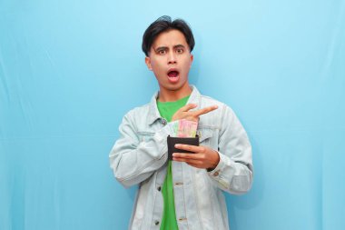 Cüzdanı elinde tutan yakışıklı Asyalı adam. Şok olmuş yüzünü gösteren bir cüzdan. Mavi arka plan.