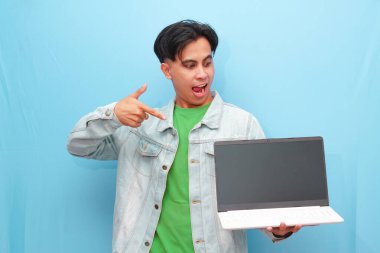 Asyalı genç adam elinde dizüstü bilgisayarla mutlu bir yüzle mavi arka planda poz veriyor.