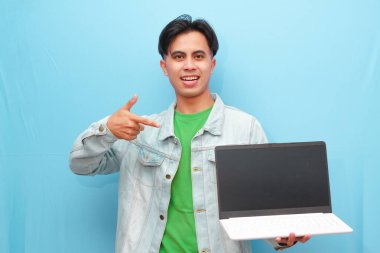 Asyalı genç adam elinde dizüstü bilgisayarla mutlu bir yüzle mavi arka planda poz veriyor.