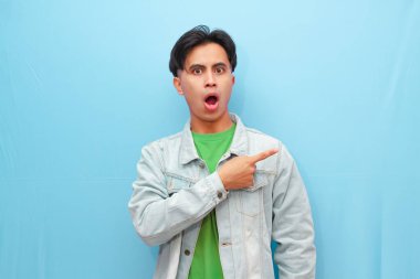 Heyecanlı Asyalı adam fantastik haberlere tepki veriyor, işaret ediyor, pankartı gösteriyor, büyük bir olay yaratıyor, şaşırmış bir şekilde gülümsüyor, mavi bir arkaplanda soyutlanıyor.