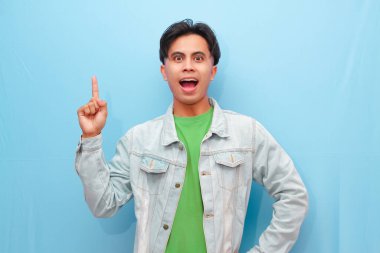 Heyecanlı Asyalı adam fantastik haberlere tepki veriyor, işaret ediyor, pankartı gösteriyor, büyük bir olay yaratıyor, şaşırmış bir şekilde gülümsüyor, mavi bir arkaplanda soyutlanıyor.