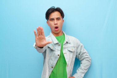 Yakışıklı Asyalı adam dur ya da hayır işareti yapıyor. Elinde ciddi bir yüz ifadesi var. Mavi arka plan.