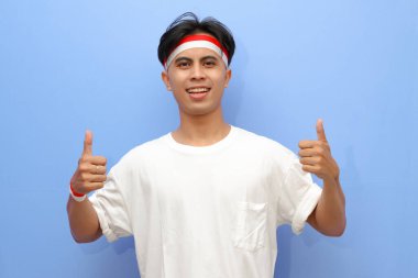 Beyaz tişörtlü Endonezyalı adam ve Endonezya bayrağı pozu. Heyecanlı bir yüz ve Endonezya 'nın bağımsızlık günü konseptiyle baş parmağını bırak.