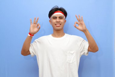 Beyaz tişörtlü Endonezyalı adam ve Endonezya bayrağı gülümseyen dostça bir jest, mükemmel bir sembol, Endonezya bağımsızlık günü konsepti ile tamam işareti yapıyor..