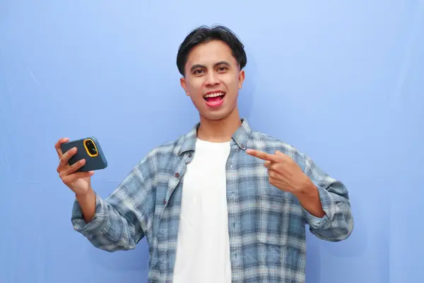 stock image Excited happy young Asian man gamer player using smartphone playing game in mobile videogame app or watching digital video stream holding cell phone isolated on blue background