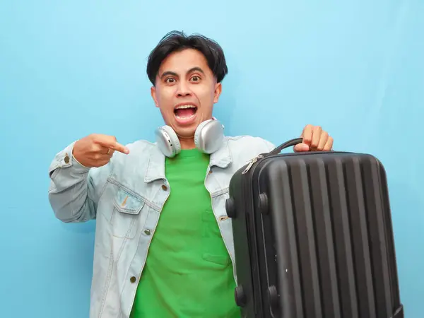 stock image Young Asian man poses carrying suitcase with happy excited gesture isolated on a blue background