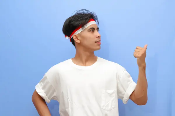 stock image Indonesian man in white shirt and Indonesian people posing pointing sideways with thumb while smiling confidently and happily, Indonesian independence day concept.