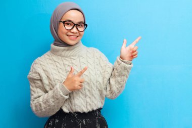 Sarı arkaplanda izole edilmiş fotokopi alanını gösteren gri kazaklı neşeli güzel Asyalı kadın. Asyalı Müslüman kadınlar fotokopi alanını işaret ediyor..