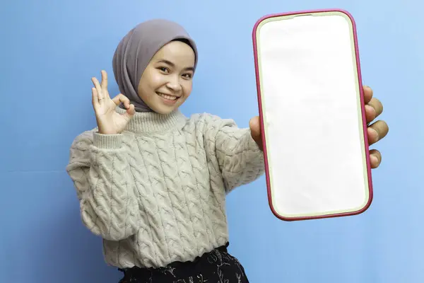 stock image Surprised young Asian woman holding smartphone with blank screen with amazed facial expression isolated on blue background.beautiful asian muslim woman showing white blank scren mobile phone with happy excited face.