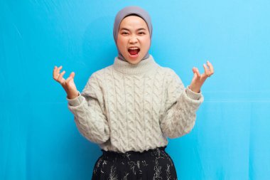 Güzel Asyalı kadın kızgın poz vererek kameraya bakıyor. Asyalı Müslüman bir kadın mavi arka planda öfkeli bir ifade sergiliyor..