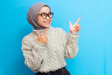 Sarı arkaplanda izole edilmiş fotokopi alanını gösteren gri kazaklı neşeli güzel Asyalı kadın. Asyalı Müslüman kadınlar fotokopi alanını işaret ediyor..