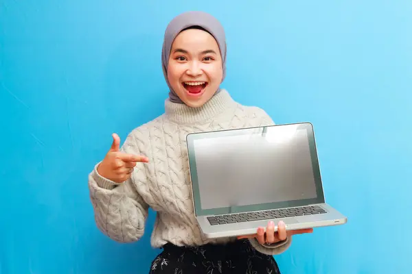 stock image Beautiful Asian Muslim woman wearing grey sweater posing by holding laptop on isolated blue background.