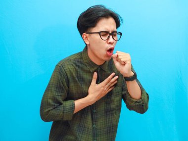 Asyalı sağlıksız bir adam boğazında ağrı, öksürük, boğaz ağrısı hissederken mavi arka planda izole edilmiş acı ifadesini gösteriyor.