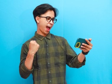 Mobil video oyunu uygulamasında akıllı telefon oyunu oynayan heyecanlı Asyalı genç oyuncu ya da izole edilmiş mavi arka planda dijital video akışını izleyen