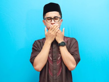 Asyalı Müslüman adam, ağzı kapalı poz veriyor mavi arka planda izole edilmiş gözleri var. Ramazan ve Bayram kavramı