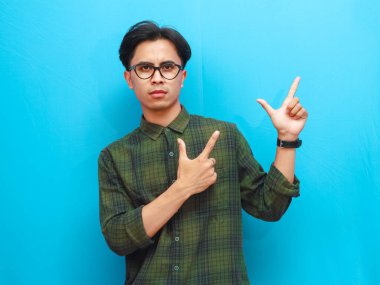 Endişeli görünen Asyalı erkek pozu fotokopi uzayını işaret ediyor.