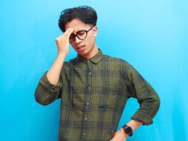 Baş ağrısı ya da migrenden muzdarip Asyalı yorgun ve genç bir adam. Beyaz arka planda yalnız kalmış umutsuz bir yüz ifadesi gösteren Asyalı bir adam.