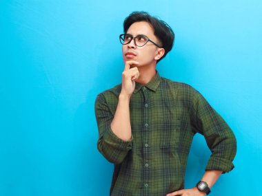 Asyalı bir adam mavi arka plana bakarak düşünme hareketi yapıyor.