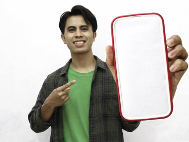 Beyaz arka planda izole edilmiş büyük model telefonları işaret ederken elinde akıllı telefon tutan heyecanlı Asyalı genç adamın portresi..