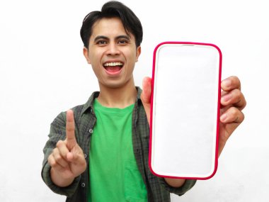 Heyecanlı genç Asyalı adam bir numarayı büyük bir akıllı telefon ekranı ile gösterirken enerjik bir şekilde parmaklarıyla gösteriyor. Reklamlar, promosyonlar ve e-ticaret içeriği için ideal, coşku ve modern teknoloji meraklısı enerji yakalamak için..