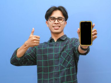 Asyalı bir adamın portresi boş bir akıllı telefon ekranı gösterirken başparmağını kaldırıyor ya da mutlu, heyecanlı bir ifadeyle iyi bir jest yapıyor, mobil teklifler, uygulamalar veya reklamlar sunmak için mükemmel..