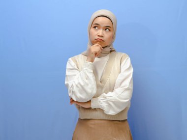 Asyalı ciddi Müslüman bir kadının portresi mavi bir arka planda el pençe içinde düşünme hareketi gösteriyor..