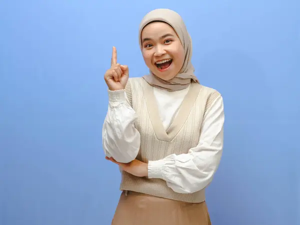 stock image Portrait of an excited Asian woman, pointing upward as if thinking of a brilliant idea, while showing a happy gesture. Isolated on a blue background.