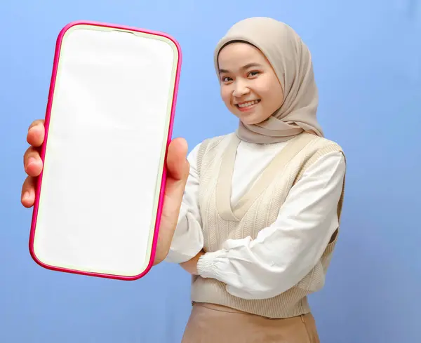 stock image Portrait of a beautiful Asian woman holding a smartphone, smiling gracefully, and showing the screen to the camera isolated blue background