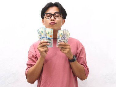 Pembe tişörtlü genç bir Asyalı elinde para tutuyordu ve beyaz arka planda mutlu bir ifadeyle bir jest yapıyordu..