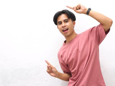 Pembe tişörtlü genç bir Asyalı beyaz arka planda şaşırtıcı bir ifadeyle yan tarafı gösteriyor..