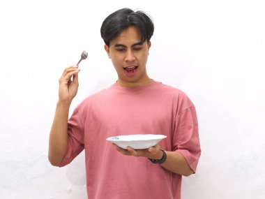 Pembe tişörtlü genç Asyalı adam elinde boş bir tabak ve çatal tutuyordu. Beyaz bir arka planda şaşkın ve heyecanlı bir ifade vardı..