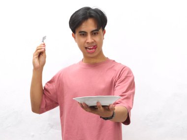 Pembe tişörtlü genç Asyalı adam elinde boş bir tabak ve çatal tutuyordu. Beyaz bir arka planda şaşkın ve heyecanlı bir ifade vardı..