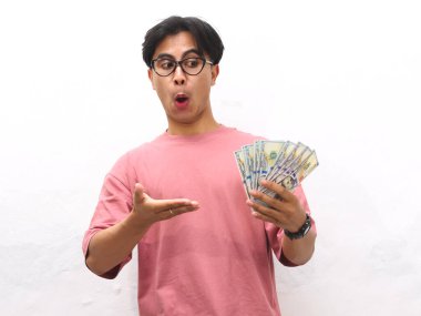 Pembe tişörtlü genç bir Asyalı 'nın portresi. Elinde para tutuyordu. Beyaz bir arkaplanda hayret verici bir ifade vardı..