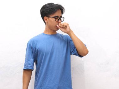 Suratında hüzünlü bir ifade olan sağlıksız genç Asyalı bir adam öksürüyor ve beyaz bir arka planda kendini iyi hissetmiyor..