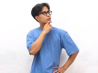 Mavi tişörtlü genç Asyalı bir adamın portresi, düşünceli bir jest gösteriyor, genç Asyalı bir adam mavi tişört giyiyor ve beyaz bir arka plana karşı düşünme hareketi gösteriyor..