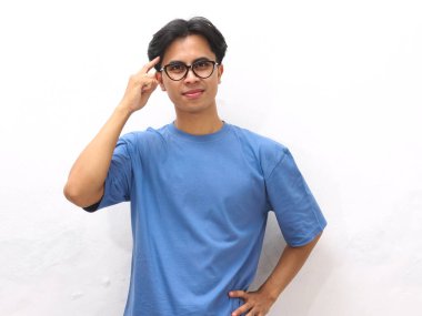 Mavi tişörtlü genç Asyalı bir adamın portresi, düşünceli bir jest gösteriyor, genç Asyalı bir adam mavi tişört giyiyor ve beyaz bir arka plana karşı düşünme hareketi gösteriyor..