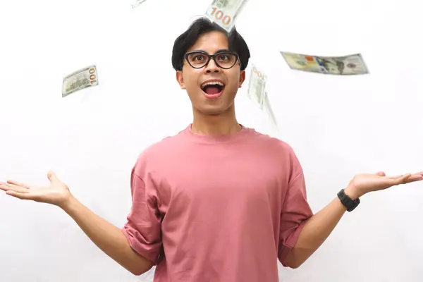 stock image Portrait of a young Asian man in a pink shirt holding money with an amazed expression on a white background.