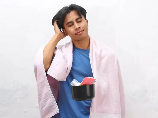 stock image Portrait of a tired Asian man holding a towel and toiletries, appearing lazy and just awake, set against a white background.