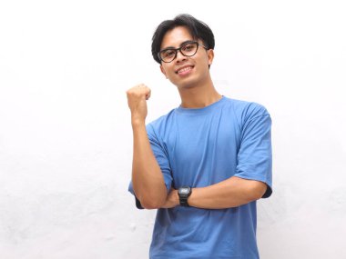 Mavi tişörtlü genç Asyalı adam başparmağıyla yan tarafı gösteriyor. Promosyon veya reklam içeriği için ideal..