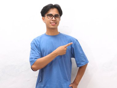 Mavi tişörtlü genç Asyalı adam boş fotokopi alanını gösteriyor. Promosyon veya reklam içeriği için ideal..