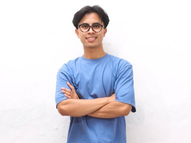 Gülümseyen, mavi tişörtlü, kolları çapraz duran, beyaz arka planda yalnız, kendinden emin, Asyalı genç bir adam.