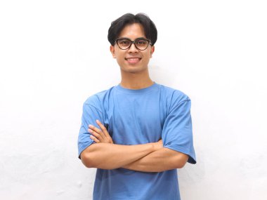 Gülümseyen, mavi tişörtlü, kolları çapraz duran, beyaz arka planda yalnız, kendinden emin, Asyalı genç bir adam.