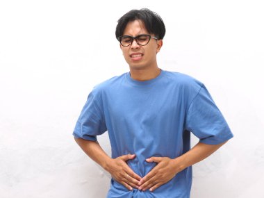 Üzgün ve acı dolu yüzü olan, midesi beyaz arka planda olan sağlıksız, genç Asyalı bir adam.