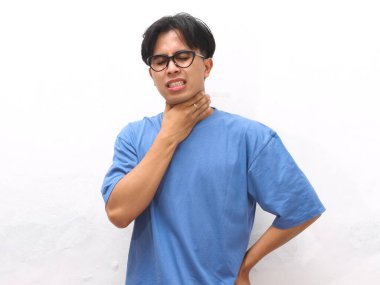 Boğazı ağrıyan, boynuna üzgün bir ifadeyle dokunan, kendini kötü hisseden, beyaz arka planda izole edilmiş, sağlıksız, genç Asyalı bir adam..
