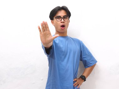 Ciddi yüzlü Asyalı genç adam elinde dur işareti yapıyor, kızgın Asyalı genç beyaz arka planda izole edilmiş, savunma jesti yapıyor, reklam amaçlarına uygun..