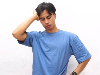 Stresli Asyalı genç adam beyaz arka planda mavi tişört giyiyor..