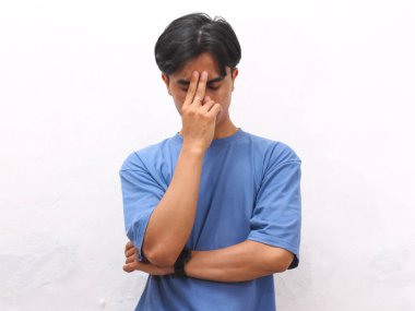 Stresli Asyalı genç adam beyaz arka planda mavi tişört giyiyor..