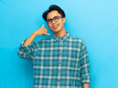 Sıradan giysiler içinde genç bir Asyalı, mavi arka planda izole bir şekilde telefonla konuşurken gülümsüyor ve poz veriyor. Reklam, promosyon ya da iletişim temaları için mükemmel..