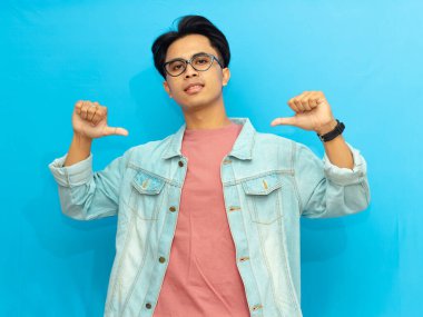 Kendine güvenen, kendine güvenen, mavi arka planda izole edilmiş, reklam ve promosyon için mükemmel bir ifadeyle kendini gösteren rahat giyimli Asyalı genç bir adam..