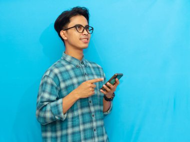 Mavi tişörtlü gülümseyen Asyalı adam elinde mavi arka planı olan bir akıllı telefon tutuyor. Teknoloji, yaşam tarzı ya da reklam kavramları için mükemmel..